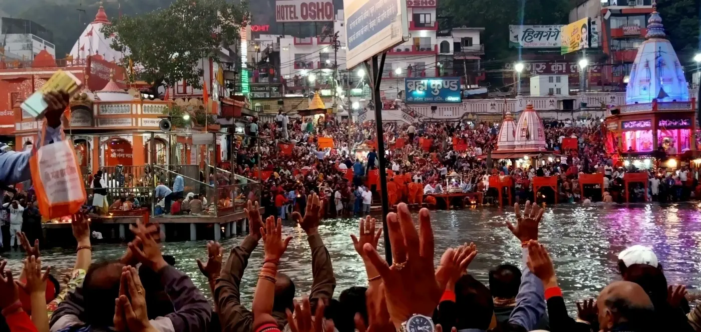 A crowd of devotees with raised hands at a riverside Ganga Aarti ceremony