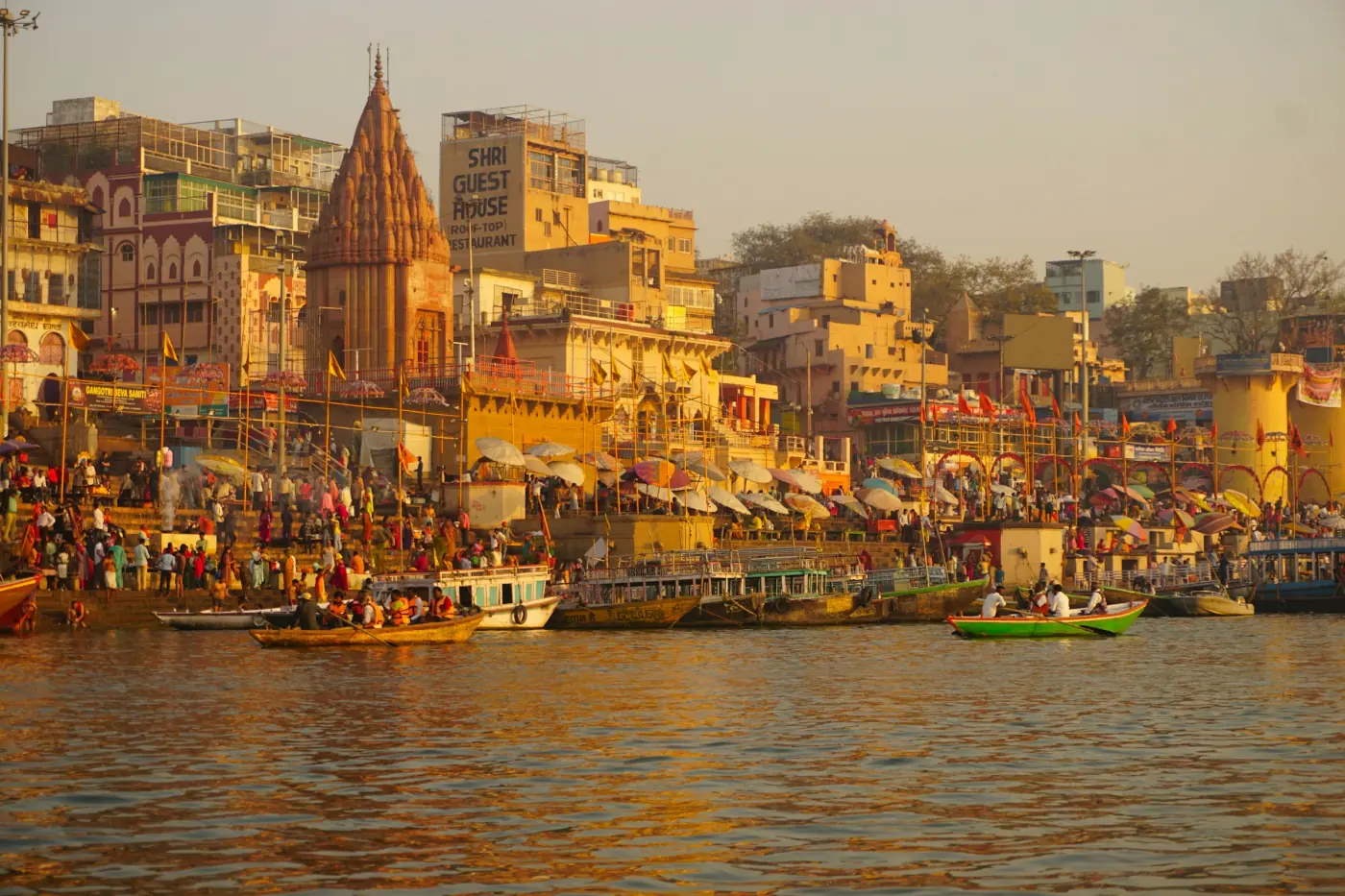 The riverfront ghats of Varanasi along the Ganga at golden hour, with boats on the river